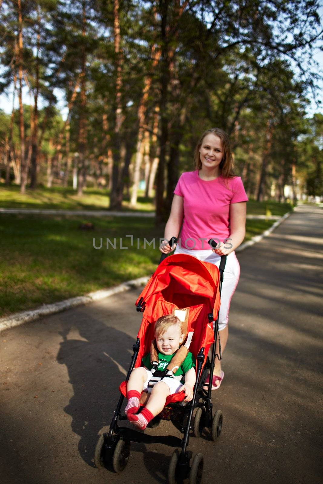 Young smiling mother with her 1 year son in the buggy walking outdoors in the park. Springday, natural colors, shallow dof (prime 35mm L optics)