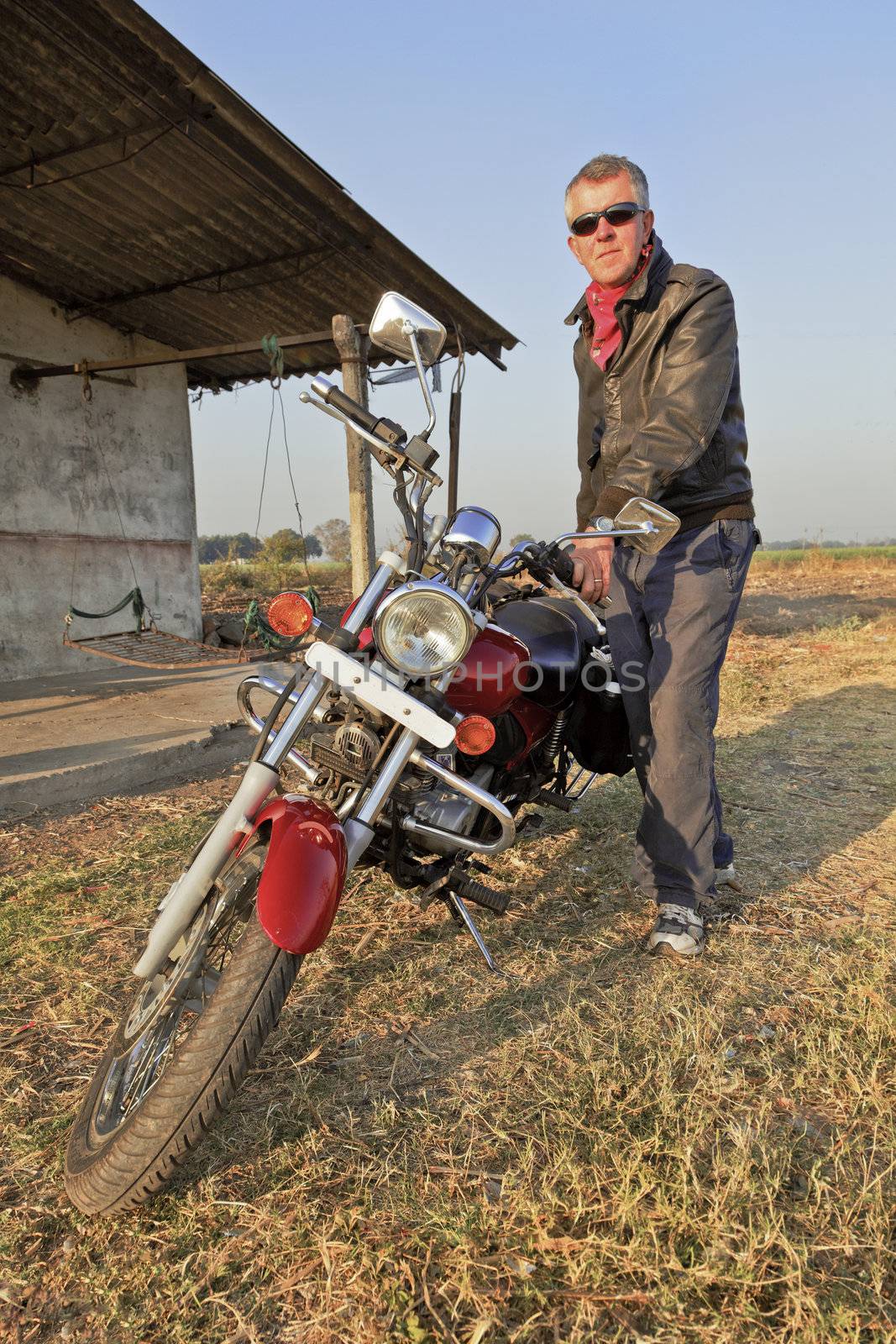 Gujarat, India, low angle view of Caucasian motor biker tourer outside a farmhouse in the country side of a northern coastal state