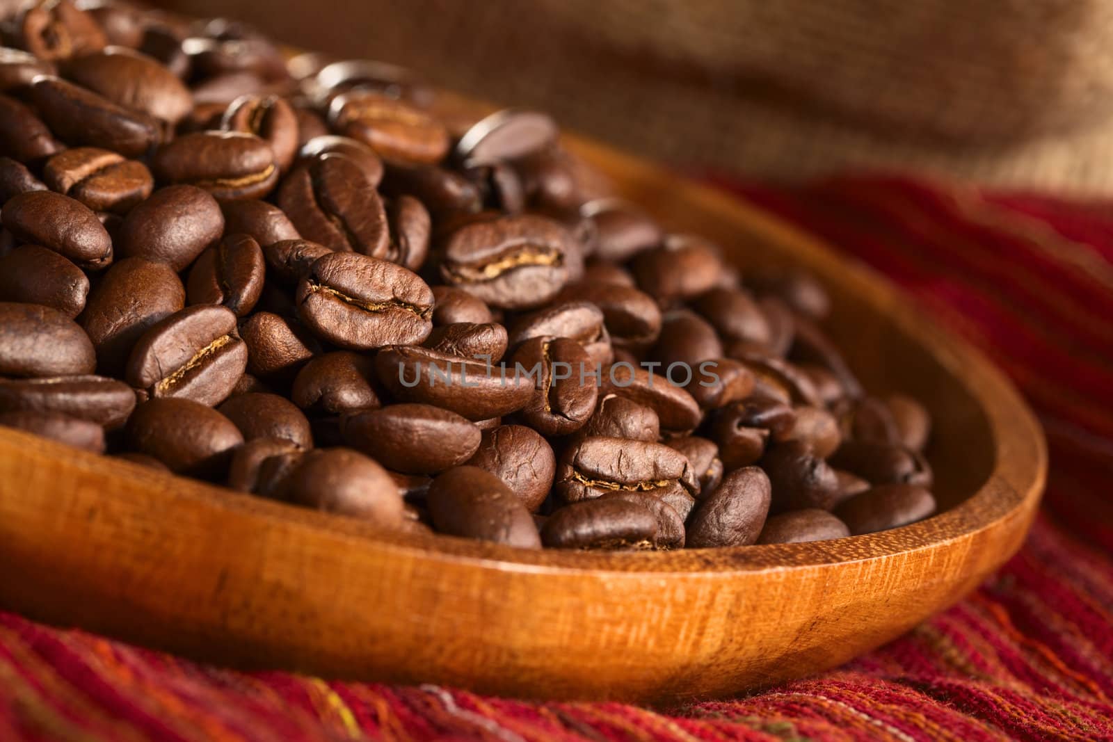 Roasted coffee beans on wooden plate on red cloth (Selective Focus, Focus one third into the coffee beans)