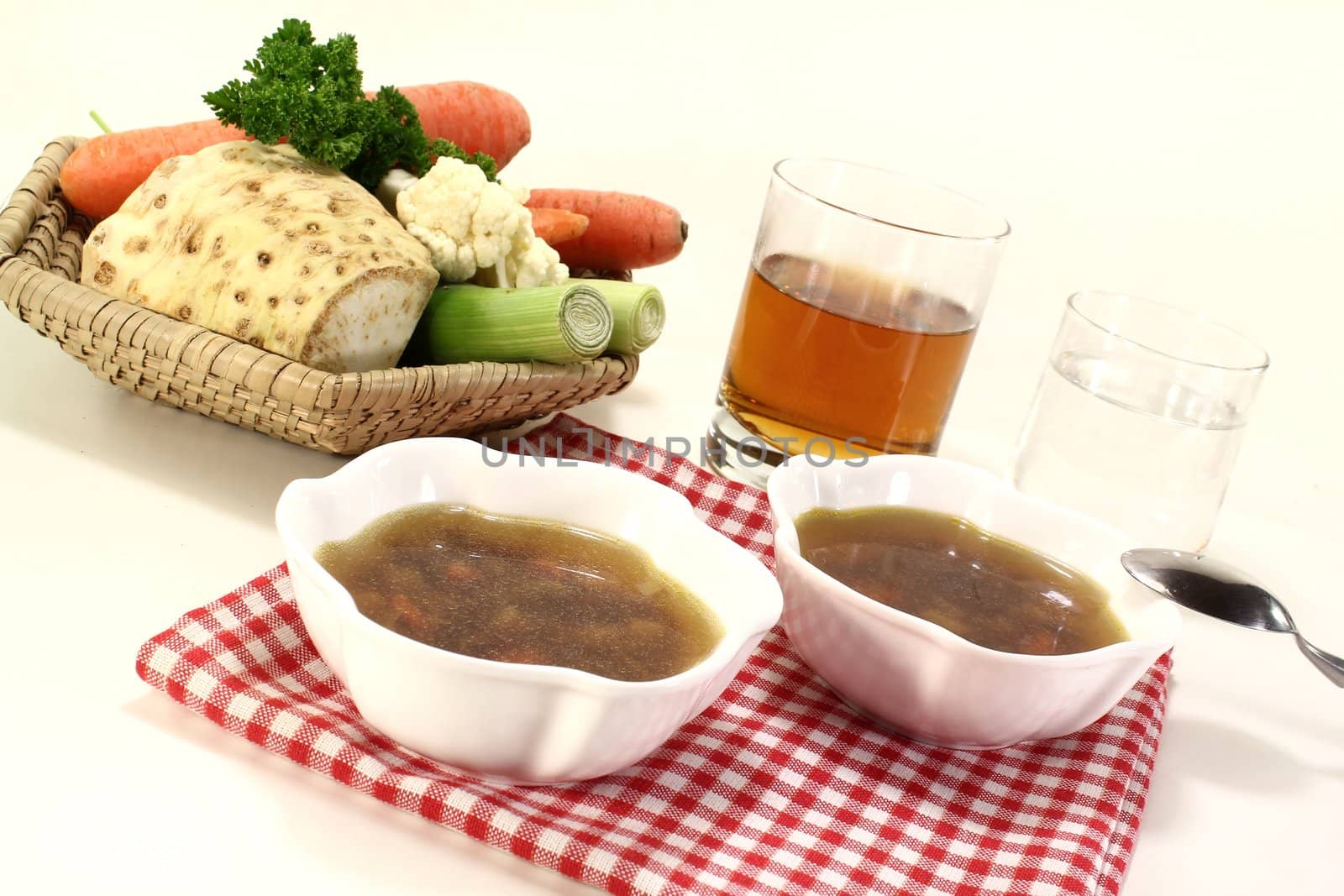 Beef consomme with greens with a glass of juice and water on a light background