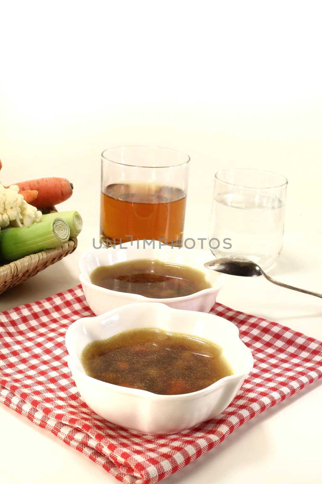 Beef consomme with vegetables on a napkin with drinks before a light background