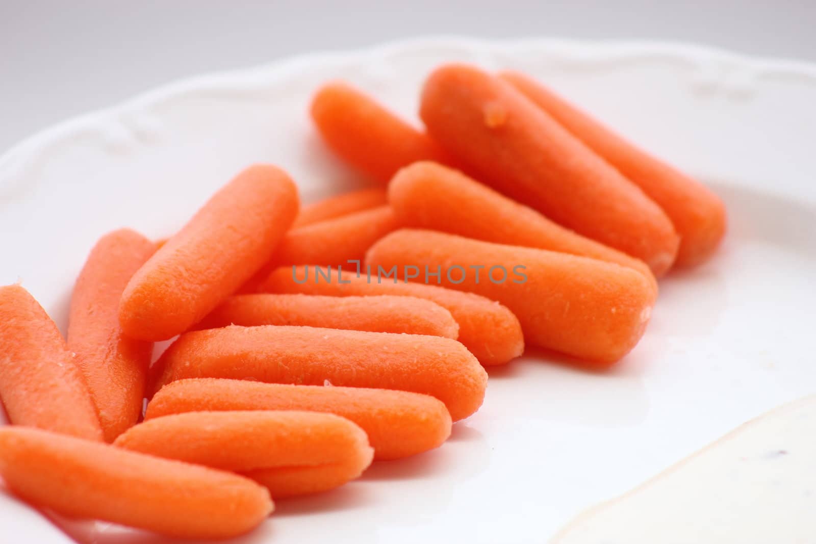 Baby Carrots on a white plate with ranch dressing on the side.