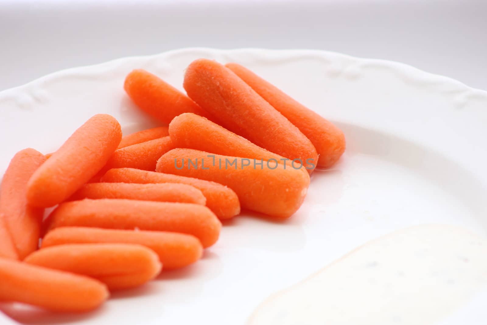 Baby carrots on a white plate with ranch dressing on the side.