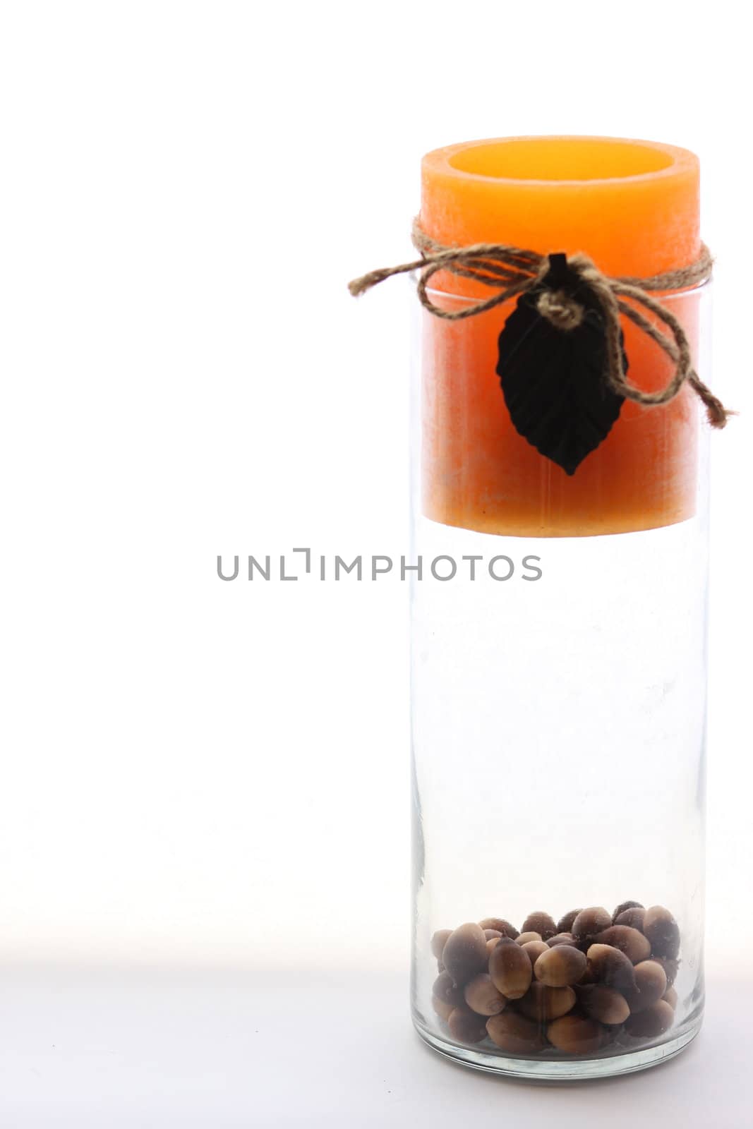 Orange candle in glass vase with acorns sitting on bottom.