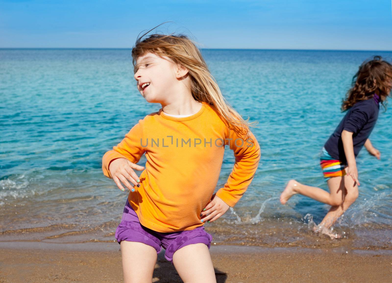 Blond kid girl dancing on the beach and her friend running on shore