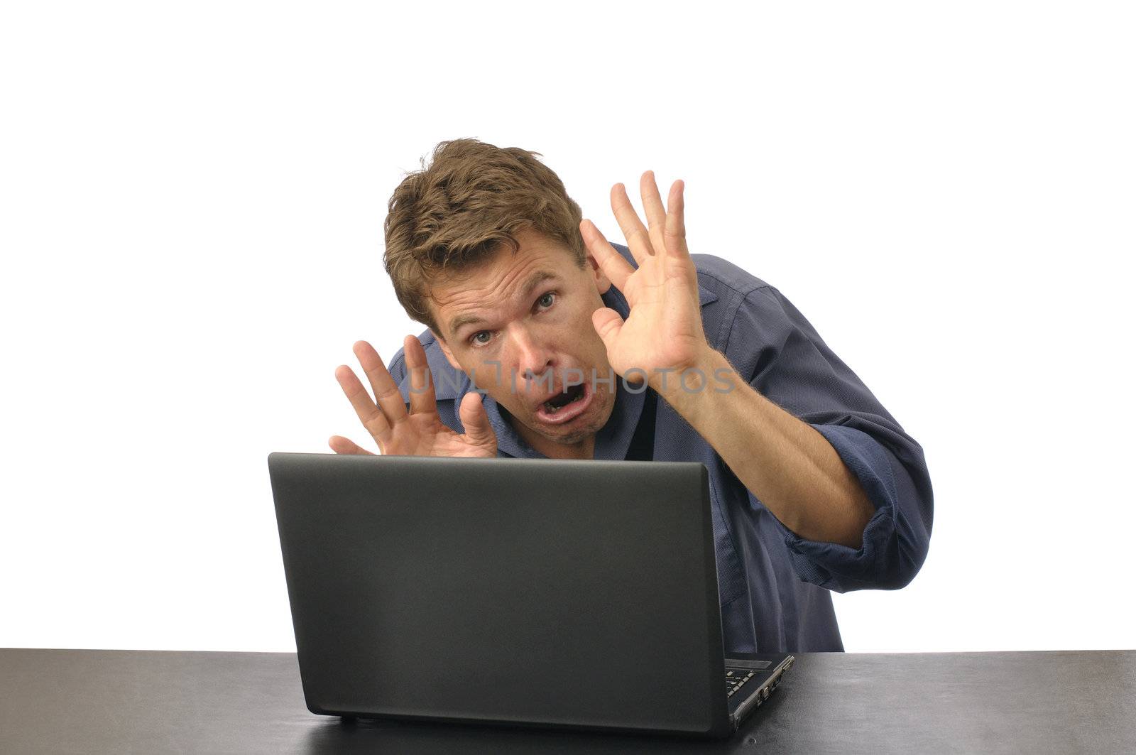 Fearful man with hands up crouches down behind computer