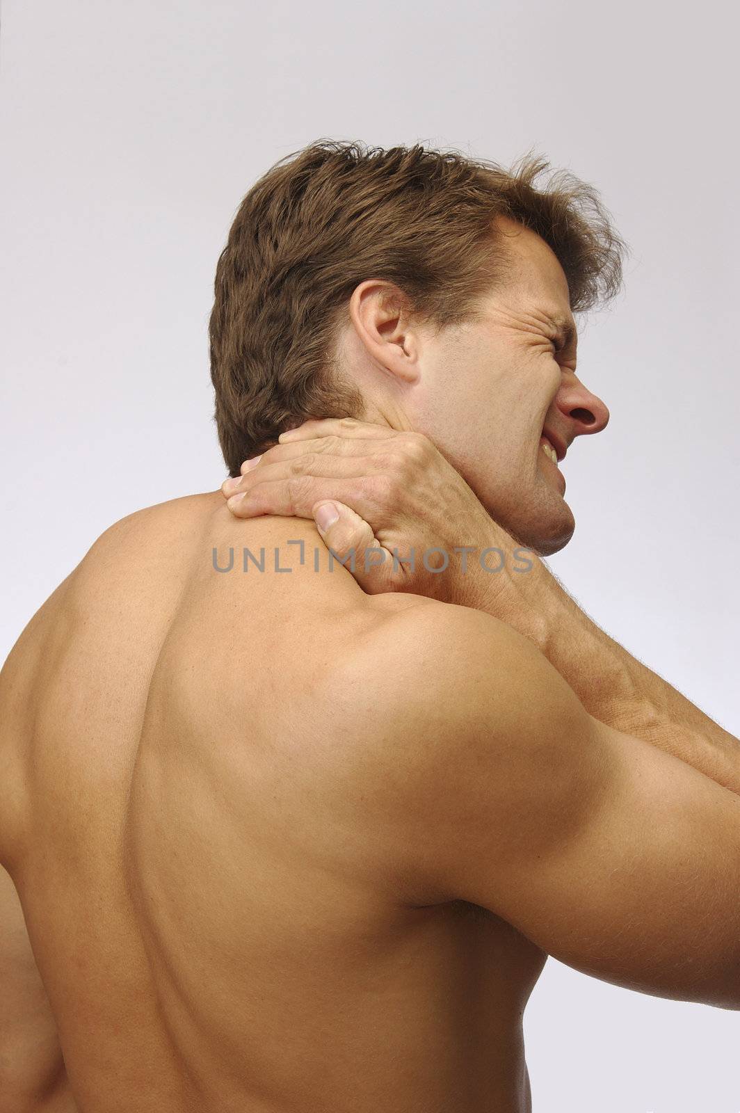 Topless athletic man holds back of neck to soothe injury