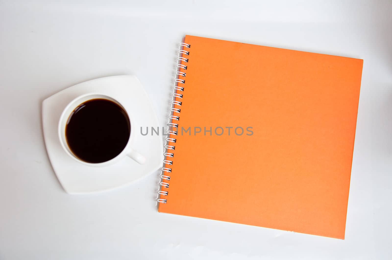 black coffee and orange notebook on white background