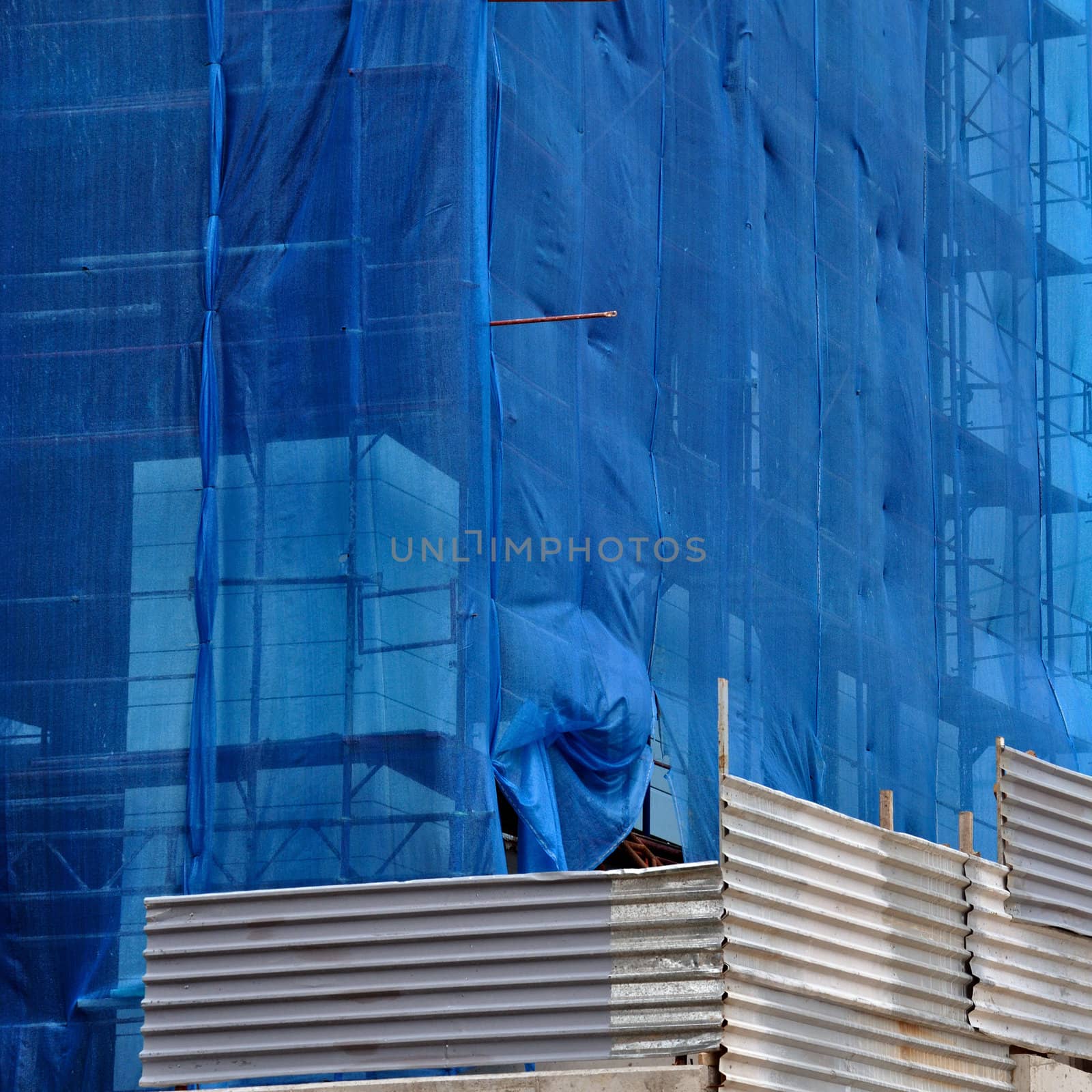 Building under debris netting at construction site. Aluminum fence and scaffold.