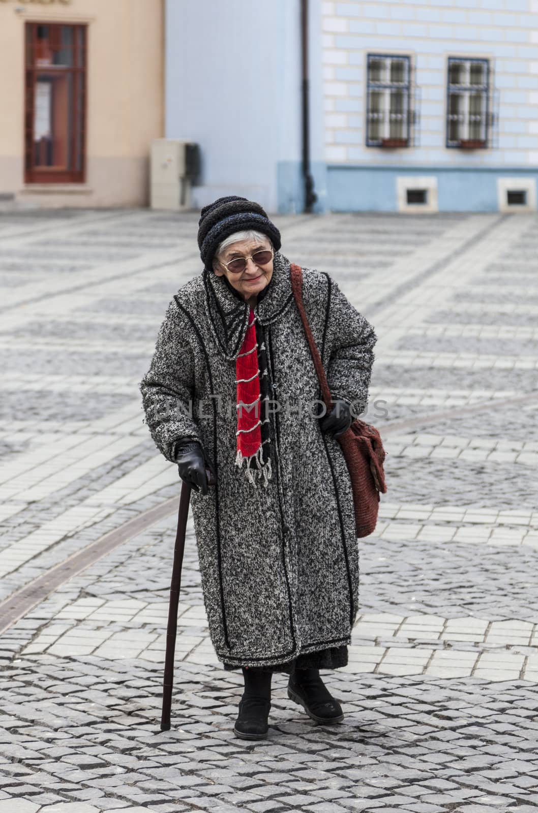 Image of a lonely senior woman walking in a paved city square.