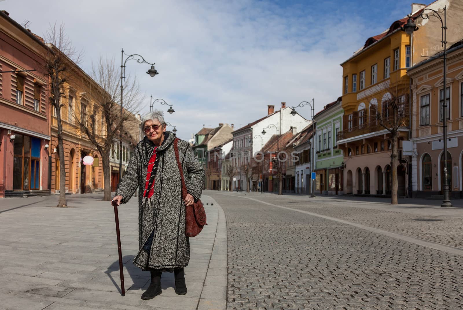Image of a lonely senior woman walking in a paved city street.