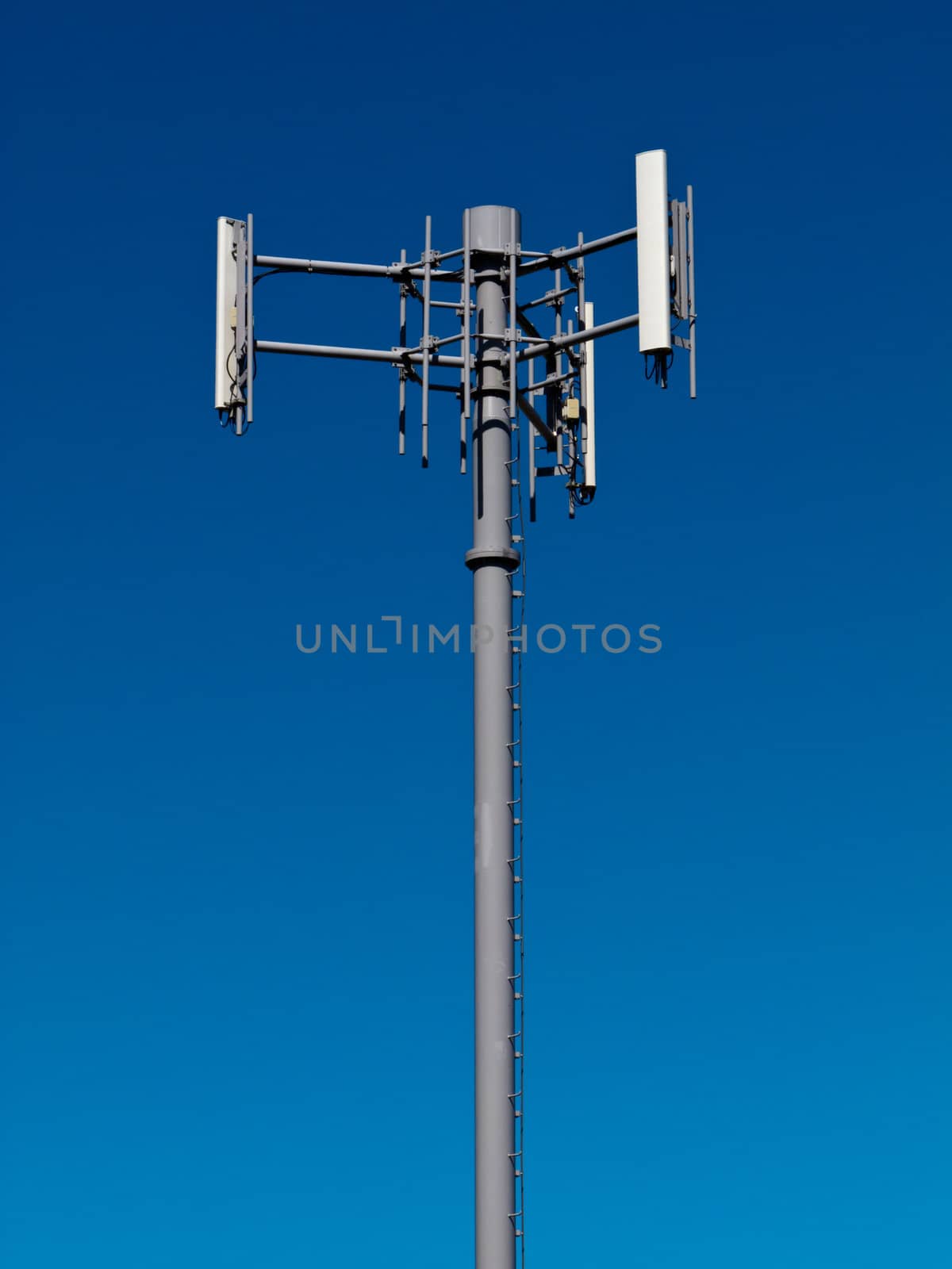 Mobile phone antennas on metal tower on blue sky by PiLens