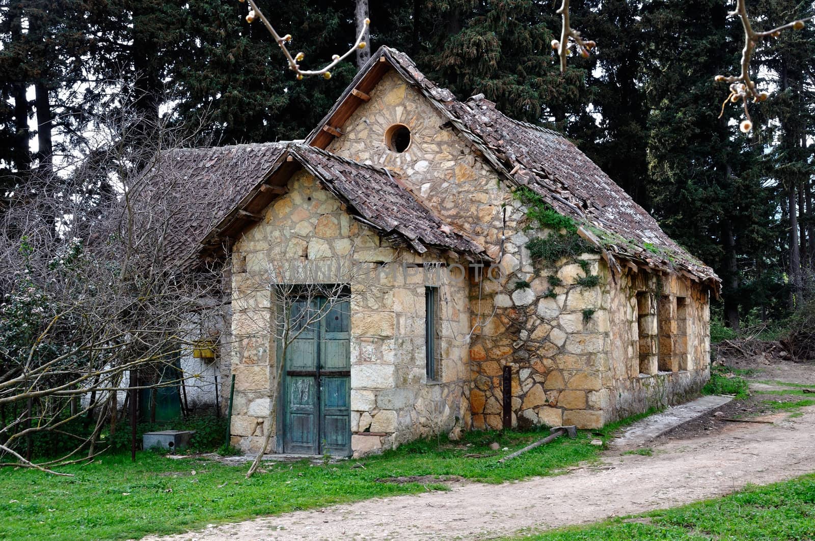 Derelict rural house with crumbling roof and dirt road in the woods.