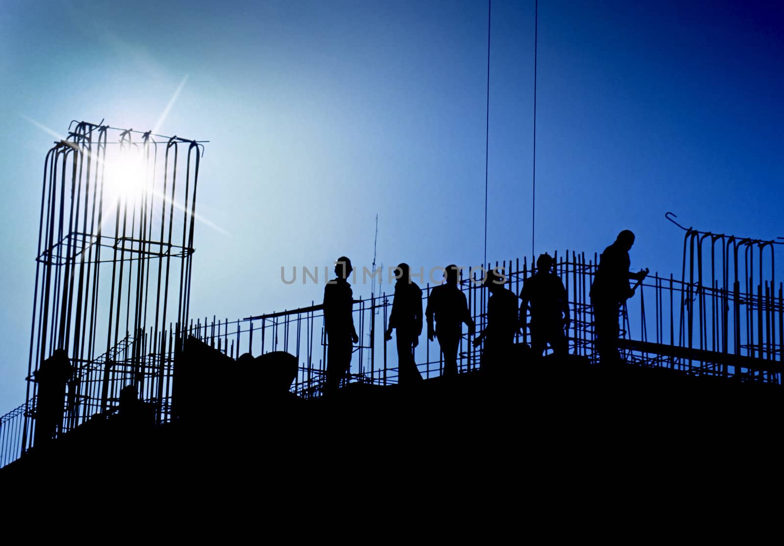Construction site with renforced concrete steel frames rising with silhouetted workers