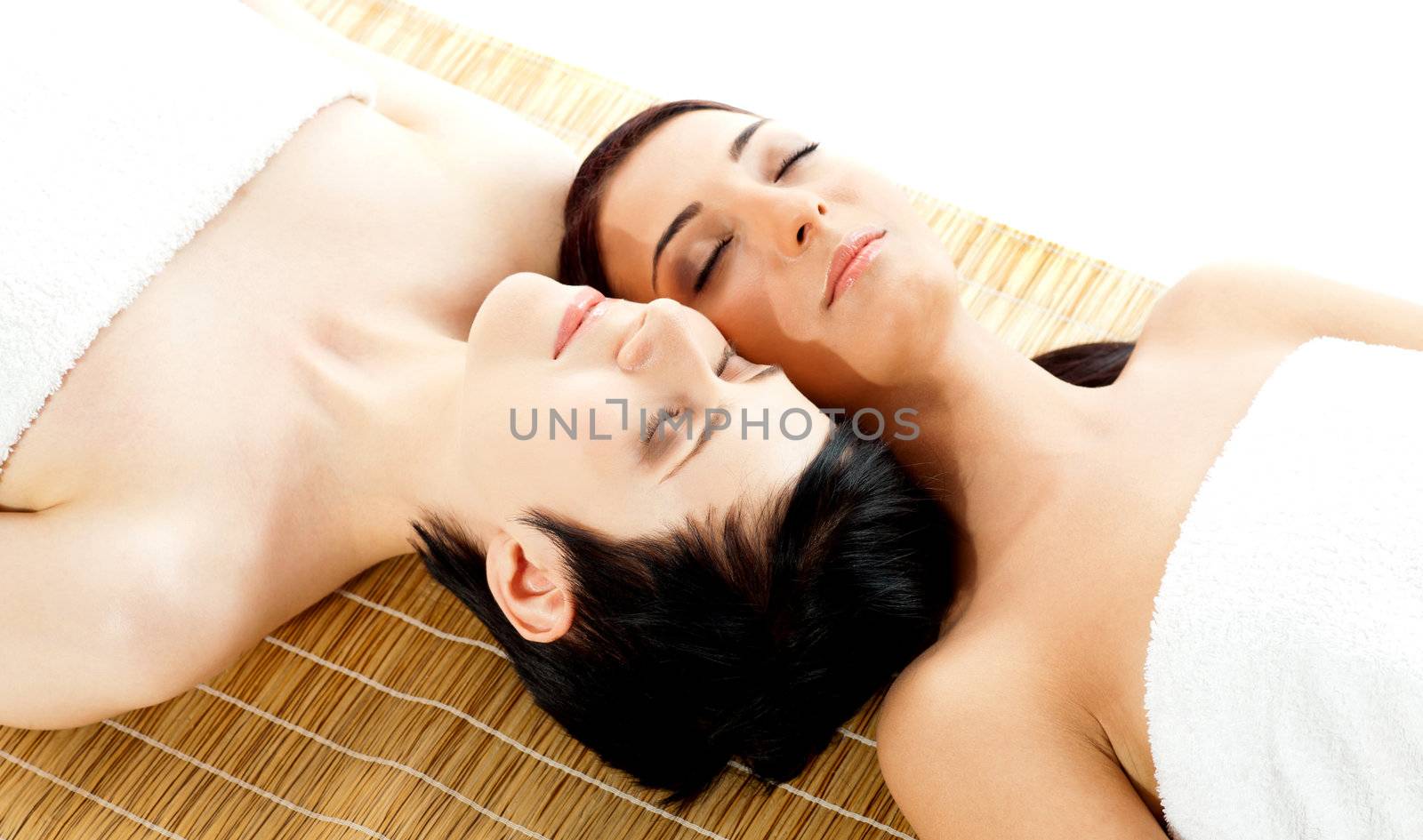 Two beautiful women friends relaxing on mat at spa salon