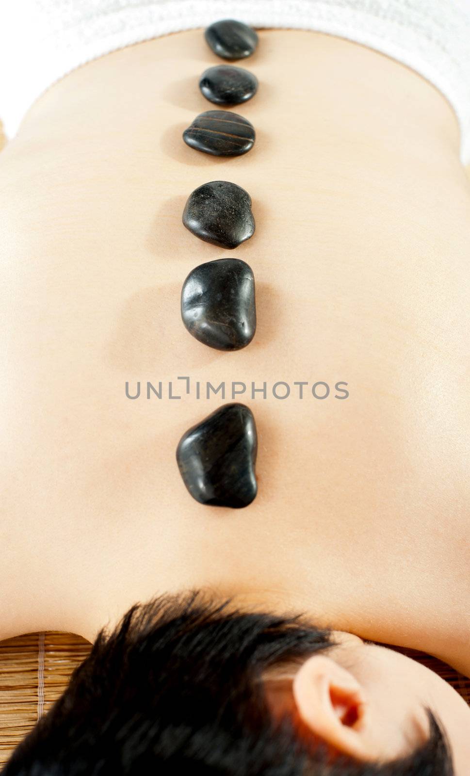 Naked woman getting spa hot stone treatment isolated over white