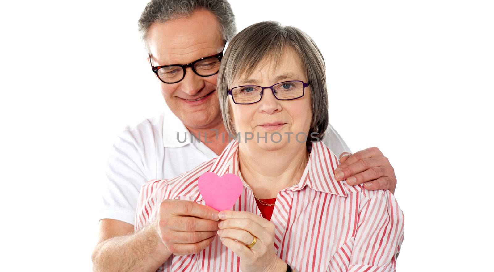 Portrait of smiling senior couple looking at camera with focus on paper heart
