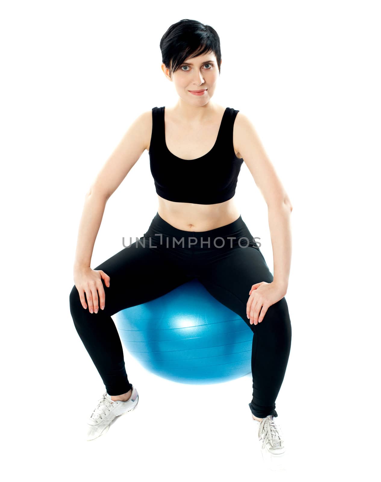 Young athlete sitting on a swiss ball at gym against white background