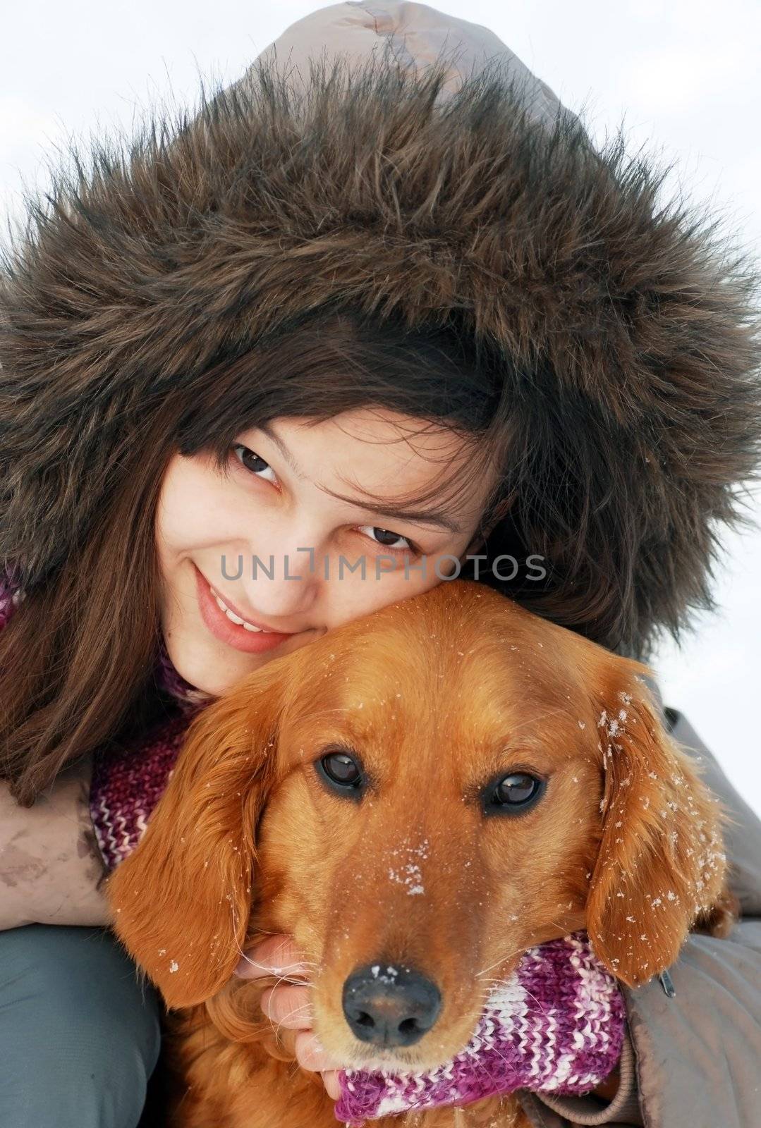 smiling teenager caucasian girl in hood hugging her dog outdoors