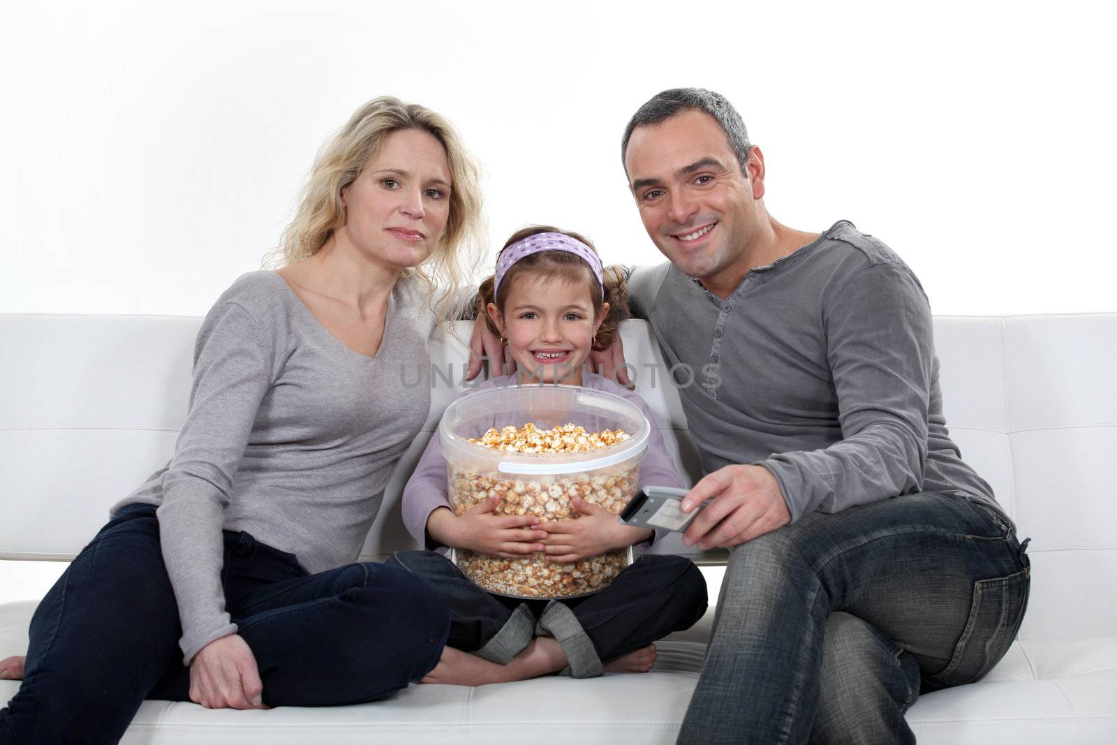 Family sitting on couch eating popcorn by phovoir