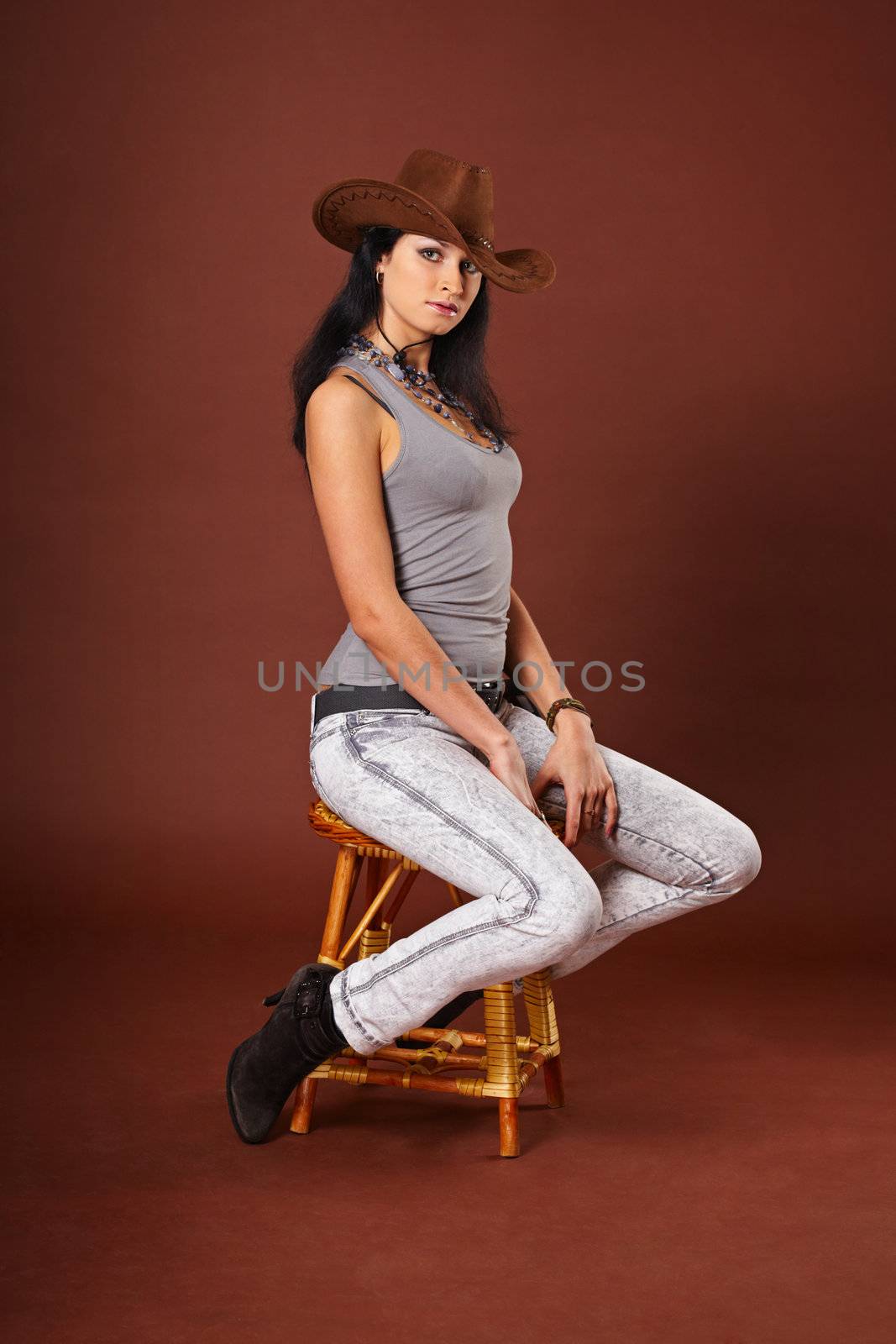 Young beautiful girl in jeans clothes and a cowboy hat, sits