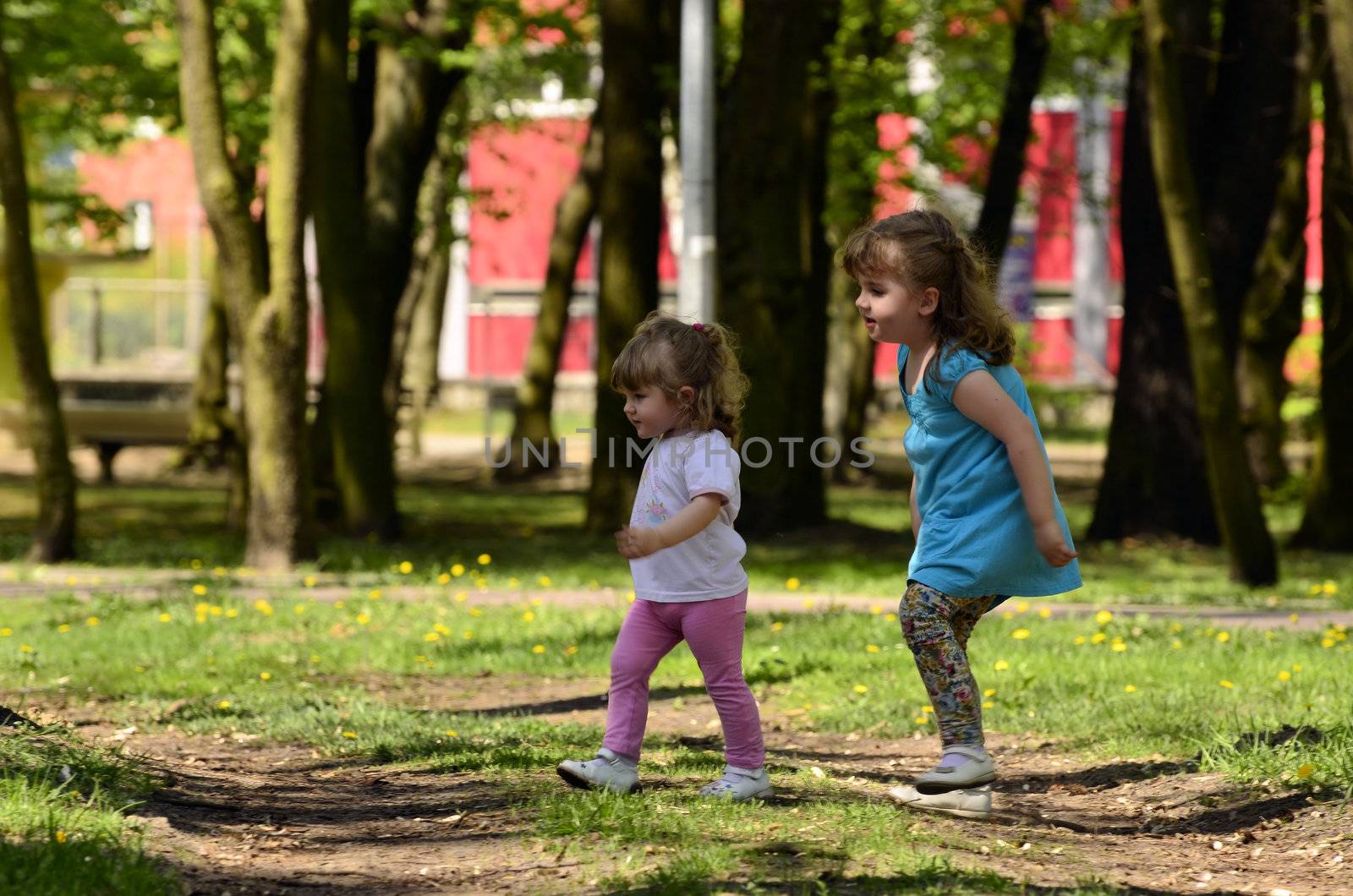 The picture shows two sisters, the elder takes care of the younger at the time having fun in the park.