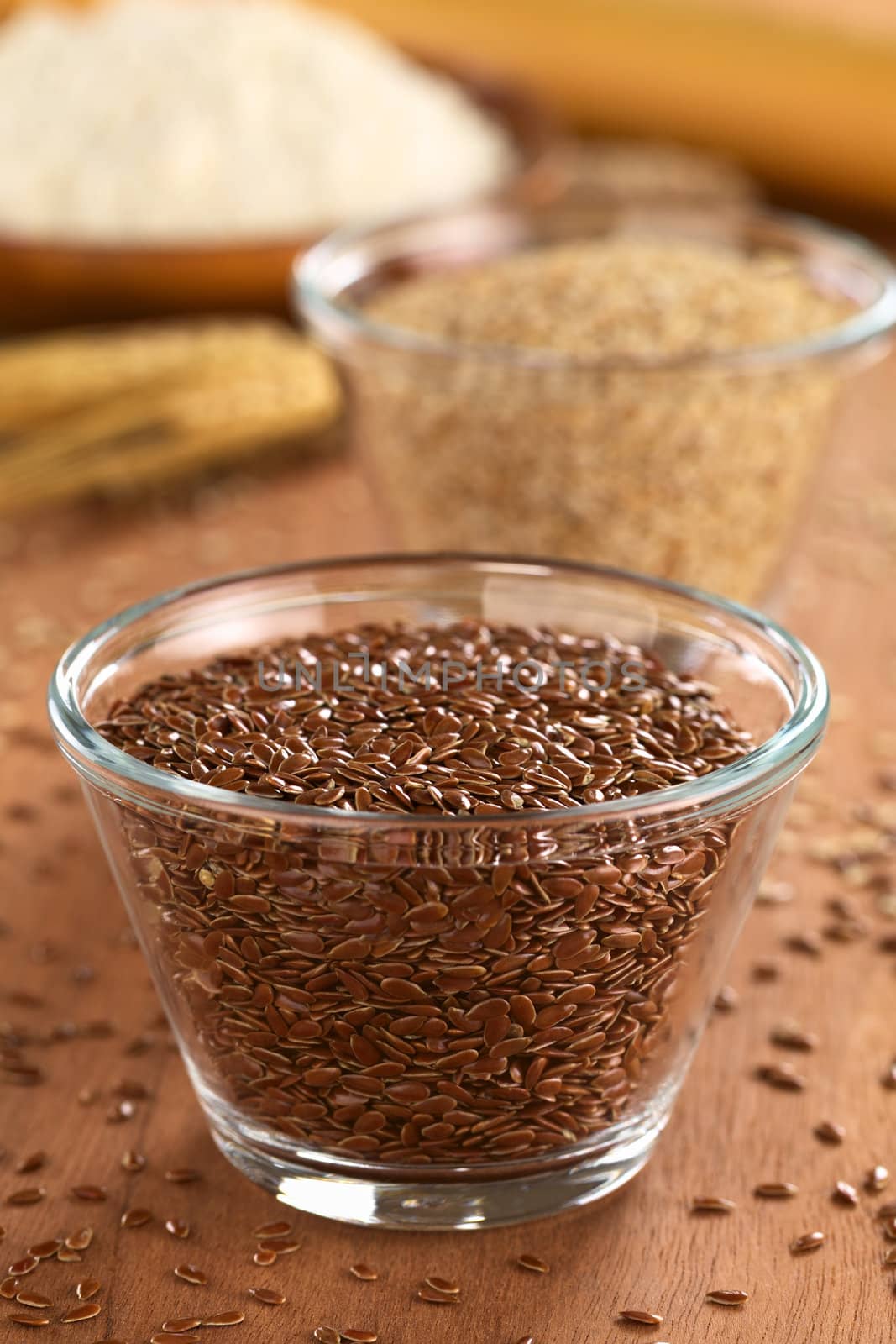 Brown flax seeds in glass bowl with sesame and flour in the back (Selective Focus, Focus one fourth into the seeds in the bowl)