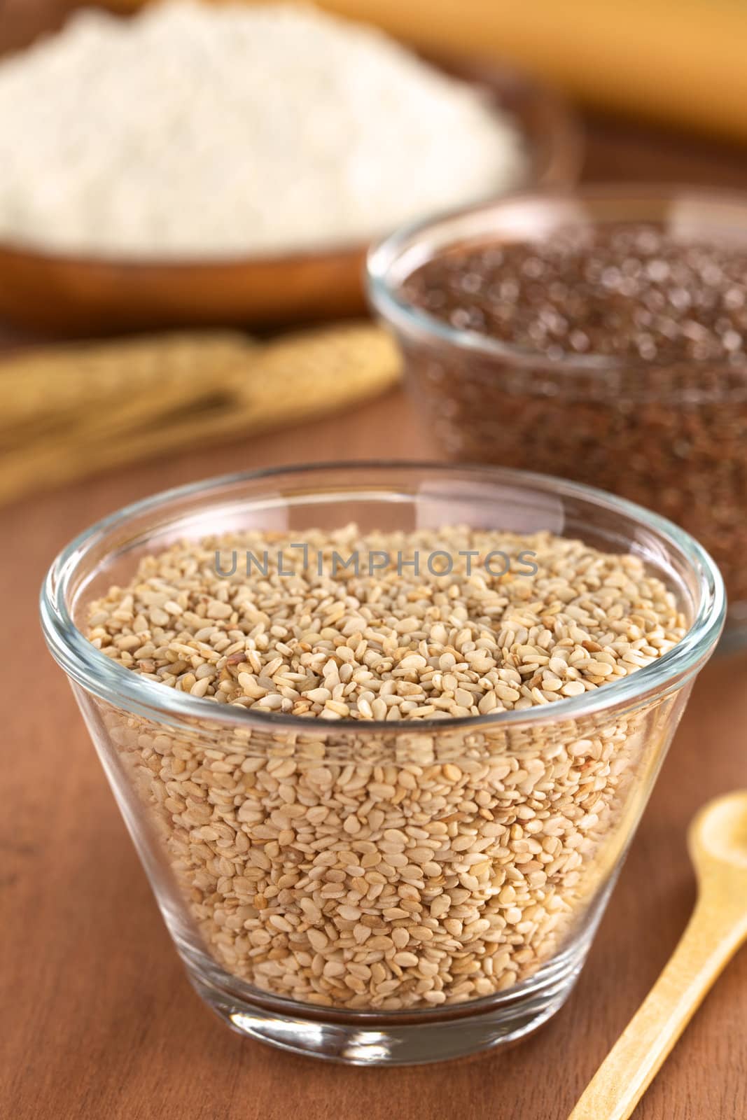 Sesame seeds in glass bowl with flax seeds and flour in the back (Selective Focus, Focus one third into the sesame seeds)