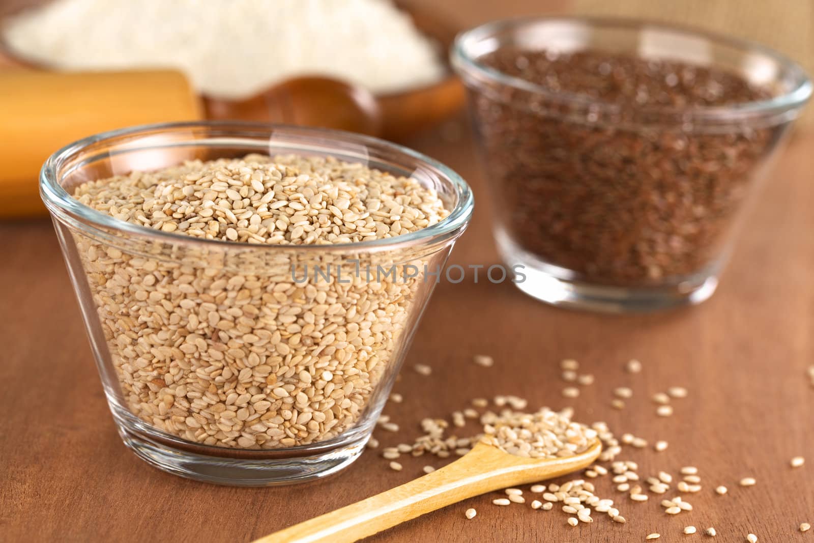 Sesame seeds in glass bowl with flax seeds and flour in the back (Selective Focus, Focus one third into the sesame seeds in the bowl)