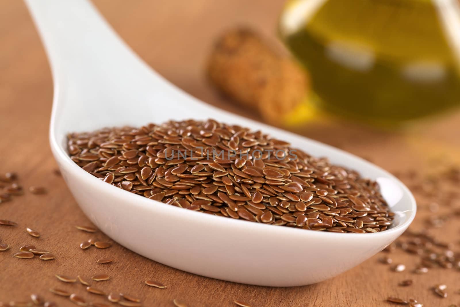 Brown flax seeds on ceramic spoon with linseed oil in the back (Selective Focus, Focus on third into the flax seeds on the spoon)