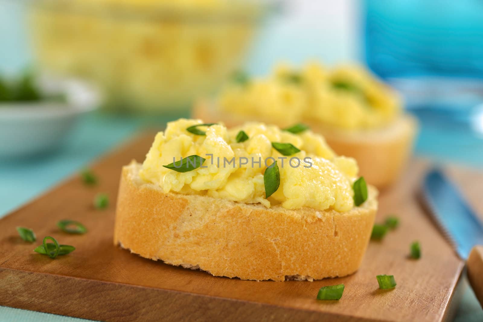 Scrambled eggs on baguette slices with green onion on wooden board (Selective Focus, Focus on the front of the first sandwich) 