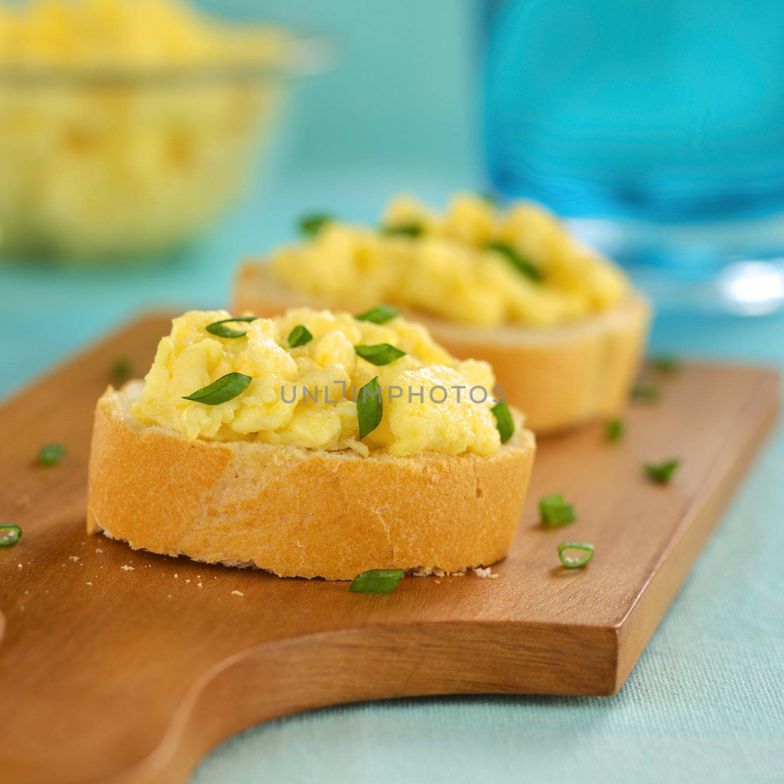 Scrambled eggs on baguette slices with green onion on wooden board (Selective Focus, Focus on the front of the first sandwich) 