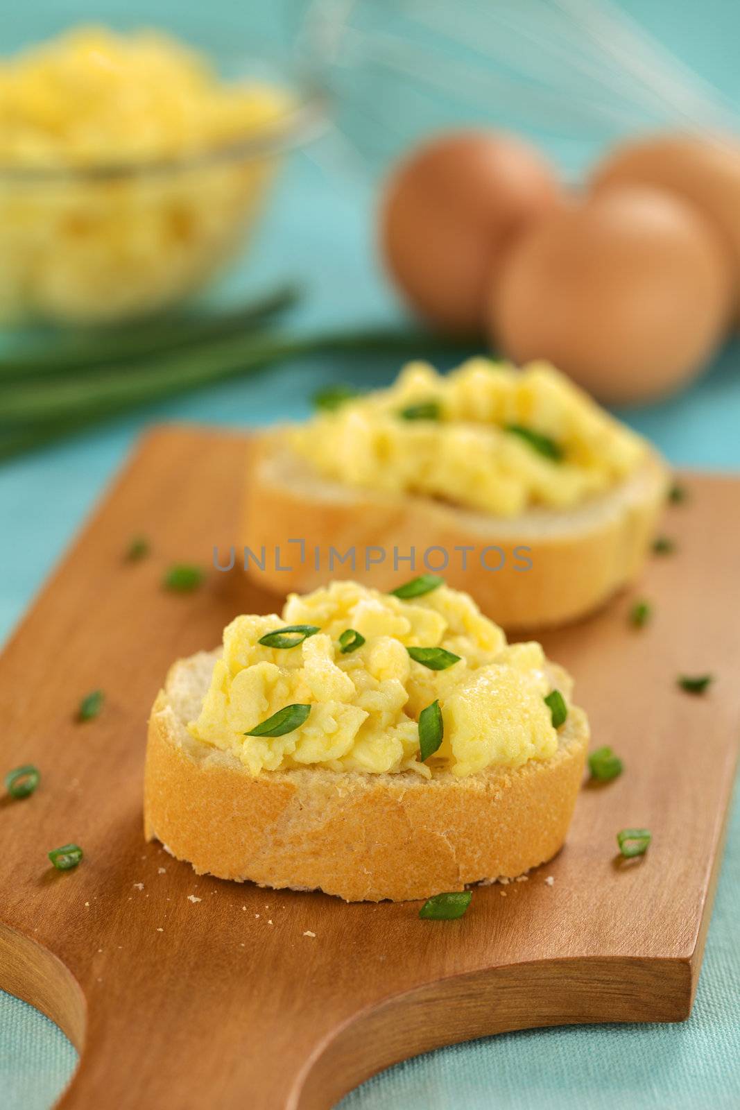 Scrambled eggs on baguette slices with green onion on wooden board (Selective Focus, Focus on the front of the first sandwich) 