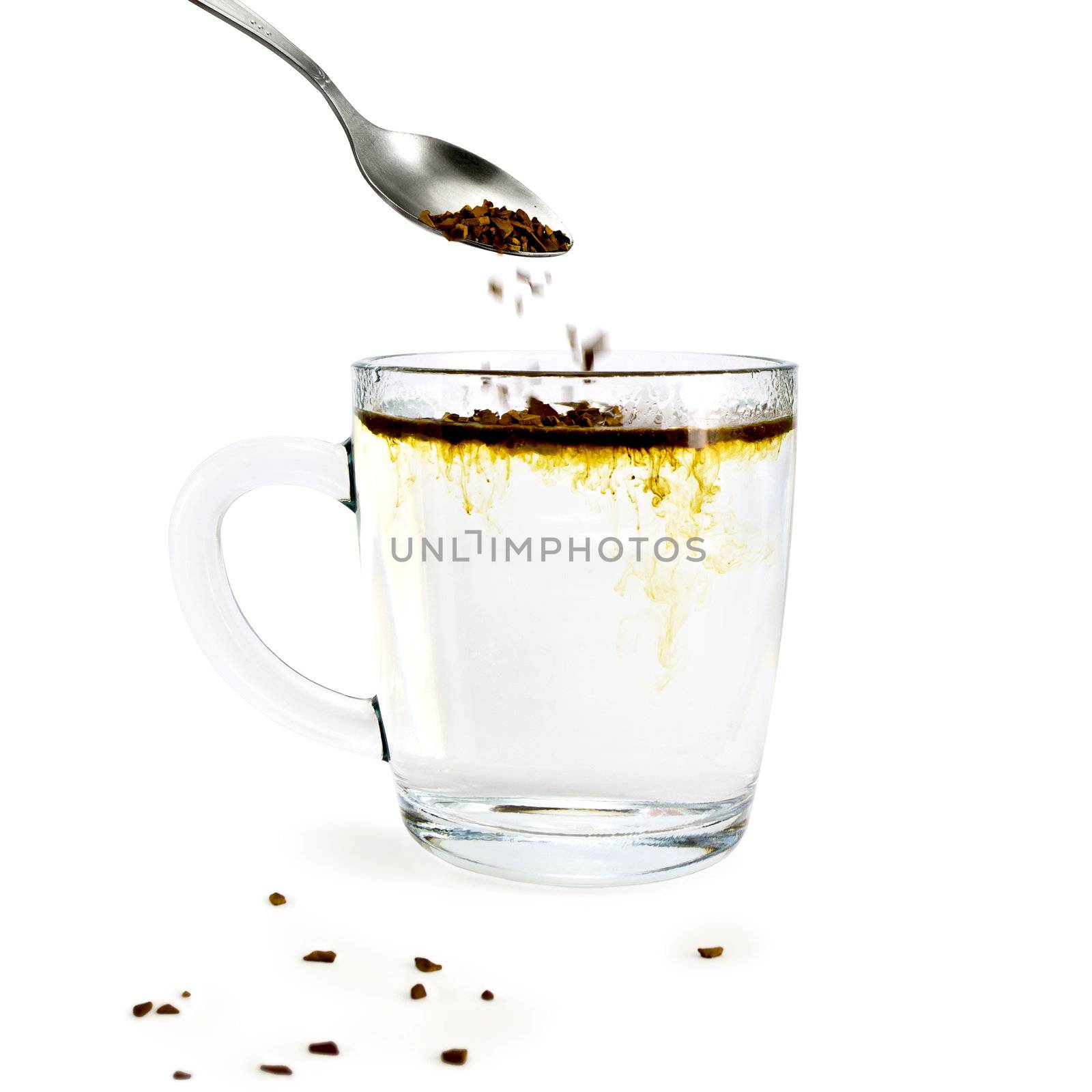 Granulated Coffee poured from a spoon into a glass mug with hot water, a few grains of coffee on the desk isolated on white background