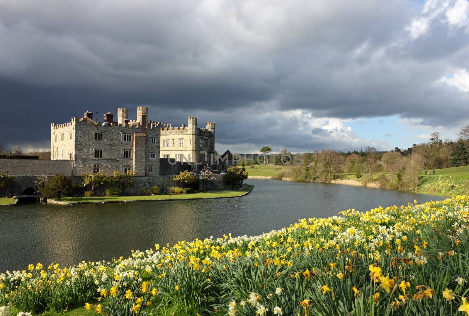 Leeds Castle in Kent, United Kingdom with blooming daffodils and dramatic sky.