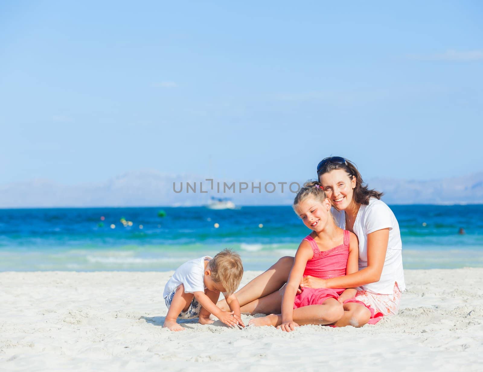 Happy family of three sitting and having fun on tropical beach