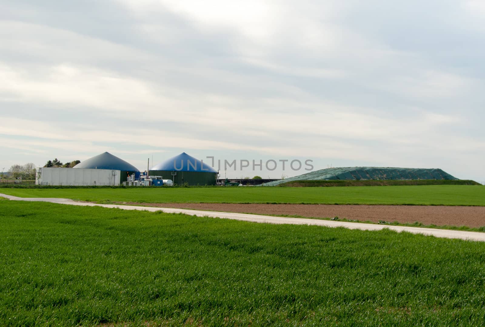 Different fermenters of a biogas plant in front of a cloudy blue sky