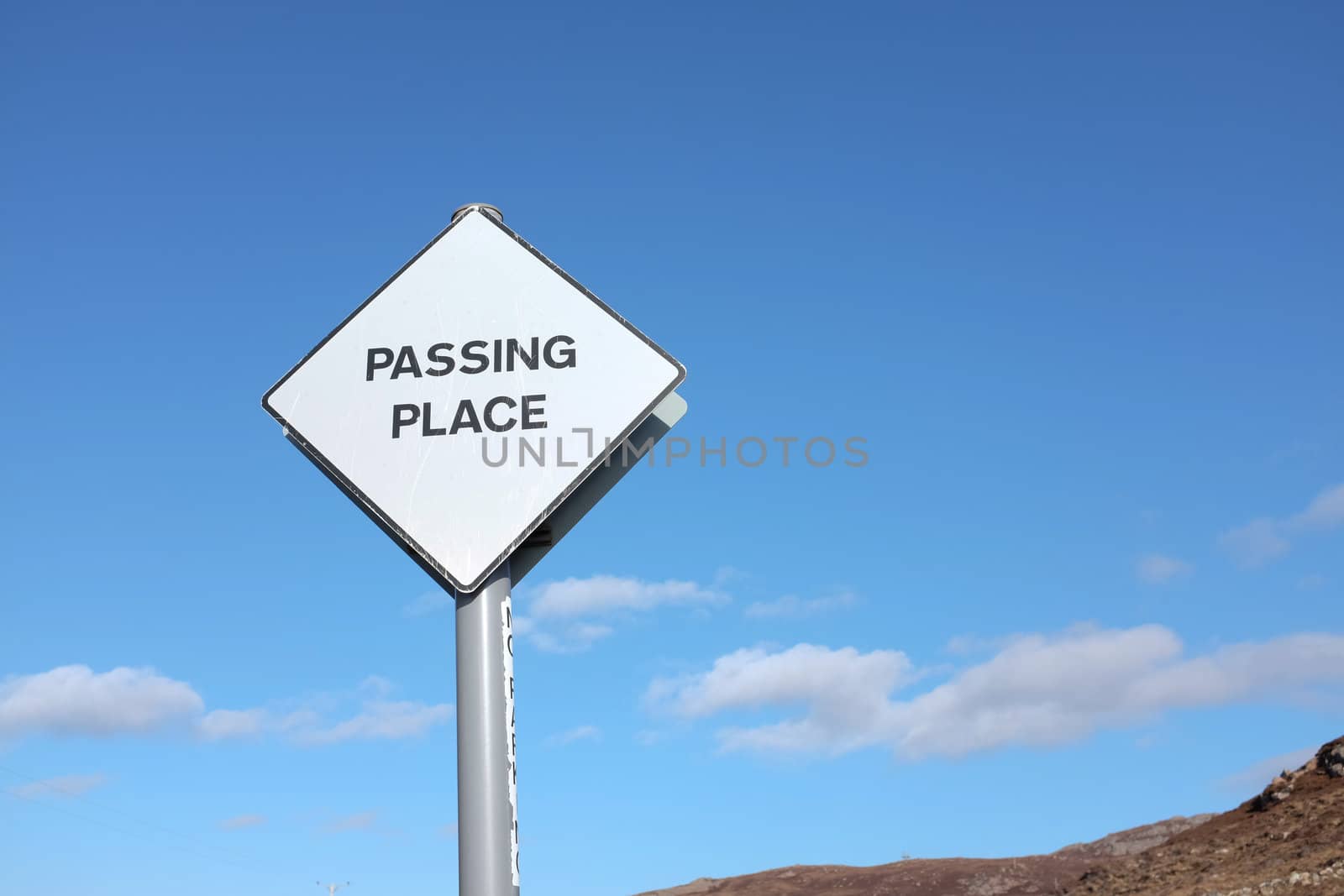 A white diamond shaped road sign with the words 'PASSING PLACE' written in black, against a blue sky with cloud,
