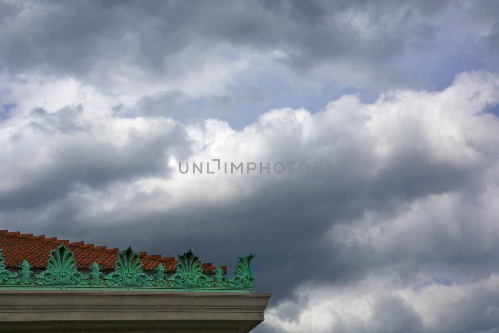 Darkening clouds over a read tile roof with green ornate decorations