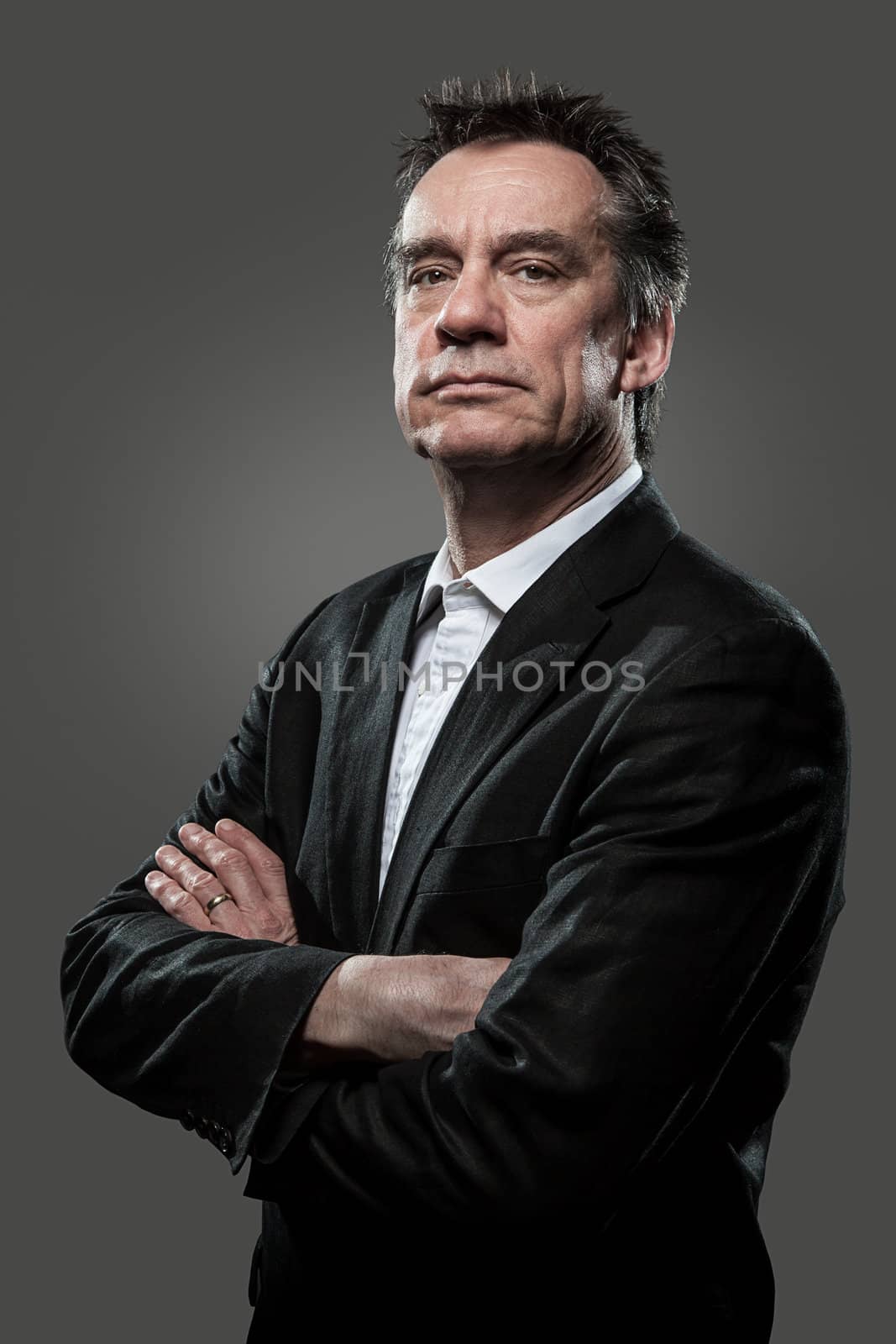 Stern Imposing Middle age Business Man with Arms Folded in Suit on Grey Background Grunge Look