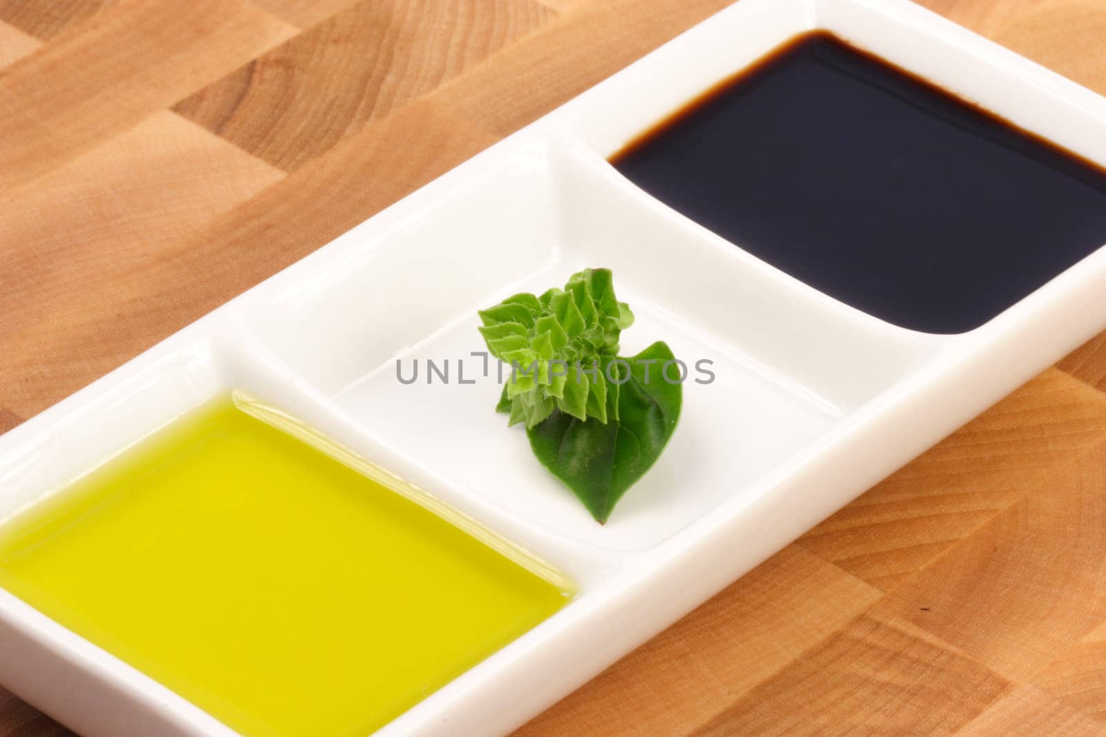 fresh first cold pressed extra virgin olive oil and balsamic vinegar on top af a fine wood cutting board garnished with basil blossom