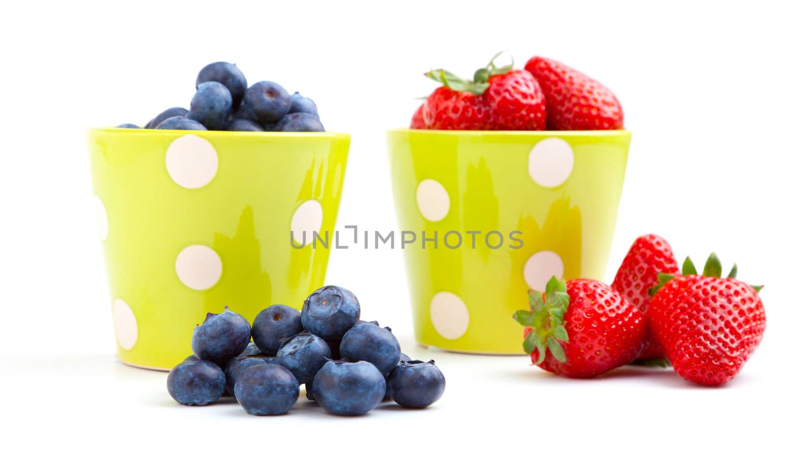 Assorted fresh picked berries in a green mug over a white background. Vertical format with reflection.