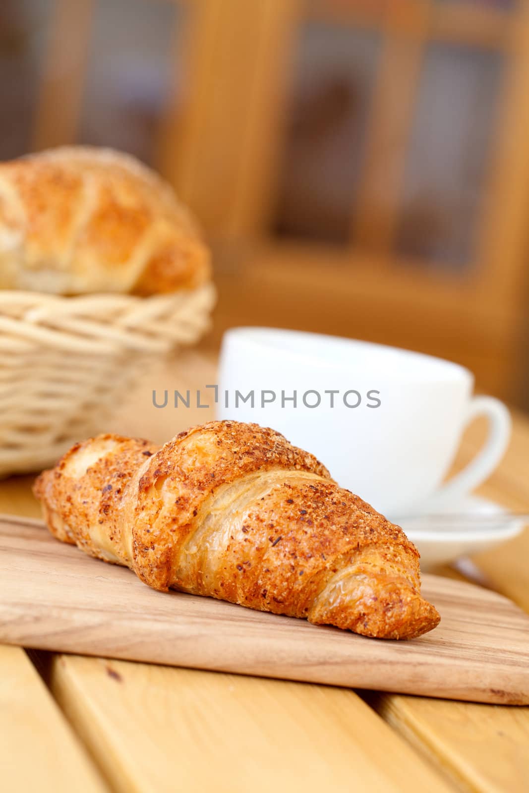 Fresh croissant and white cup coffee, on a wooden table by motorolka