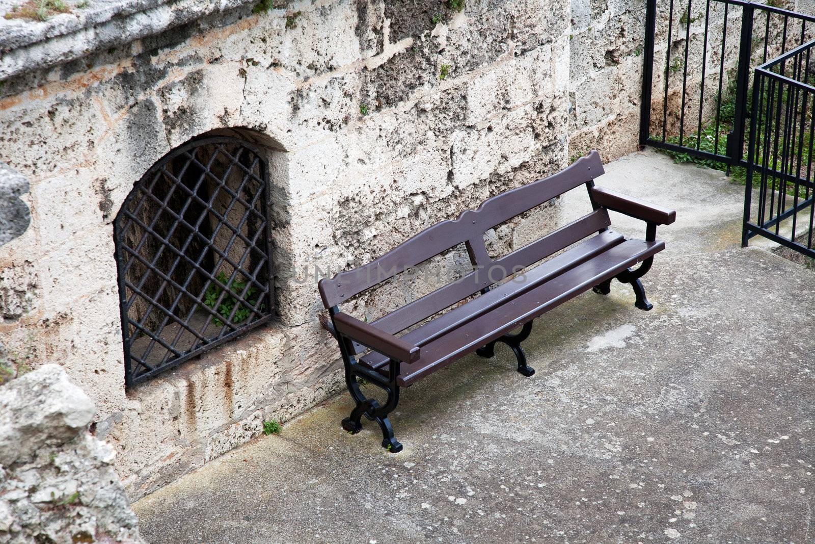 Lonely bench next to window with metal grate