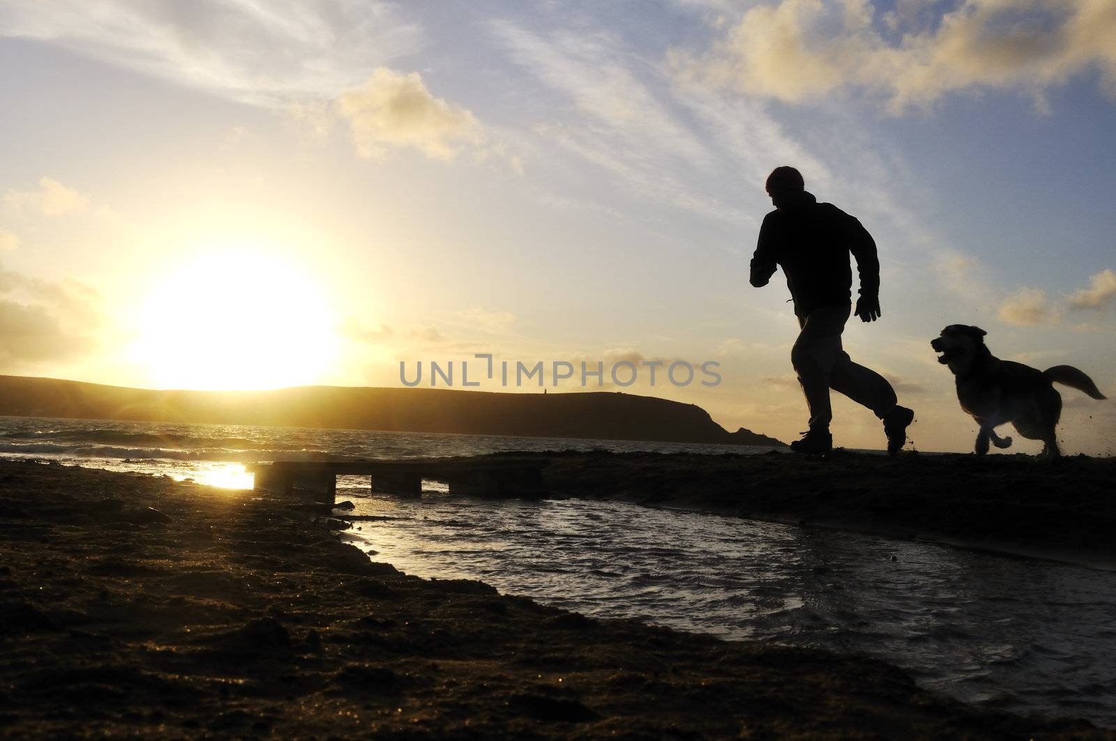 Silhouette of one man running on the beach with his dog.