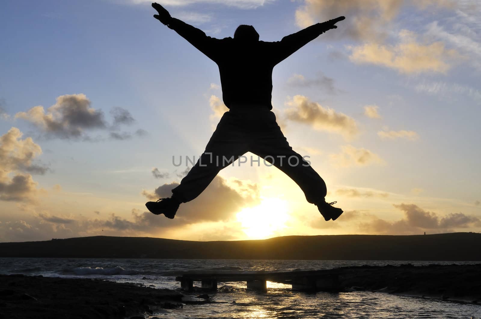 Silhouette of one man jumping over water at the beach.