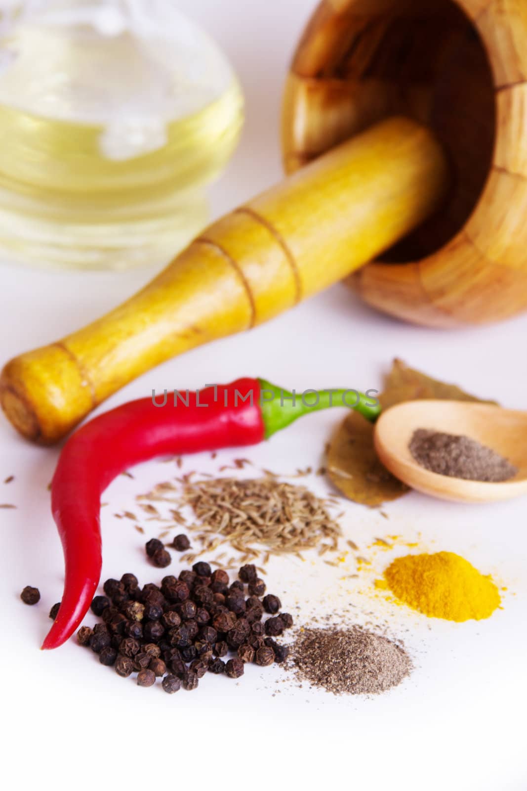 Mortar with pestle, variety of spices and oil over white