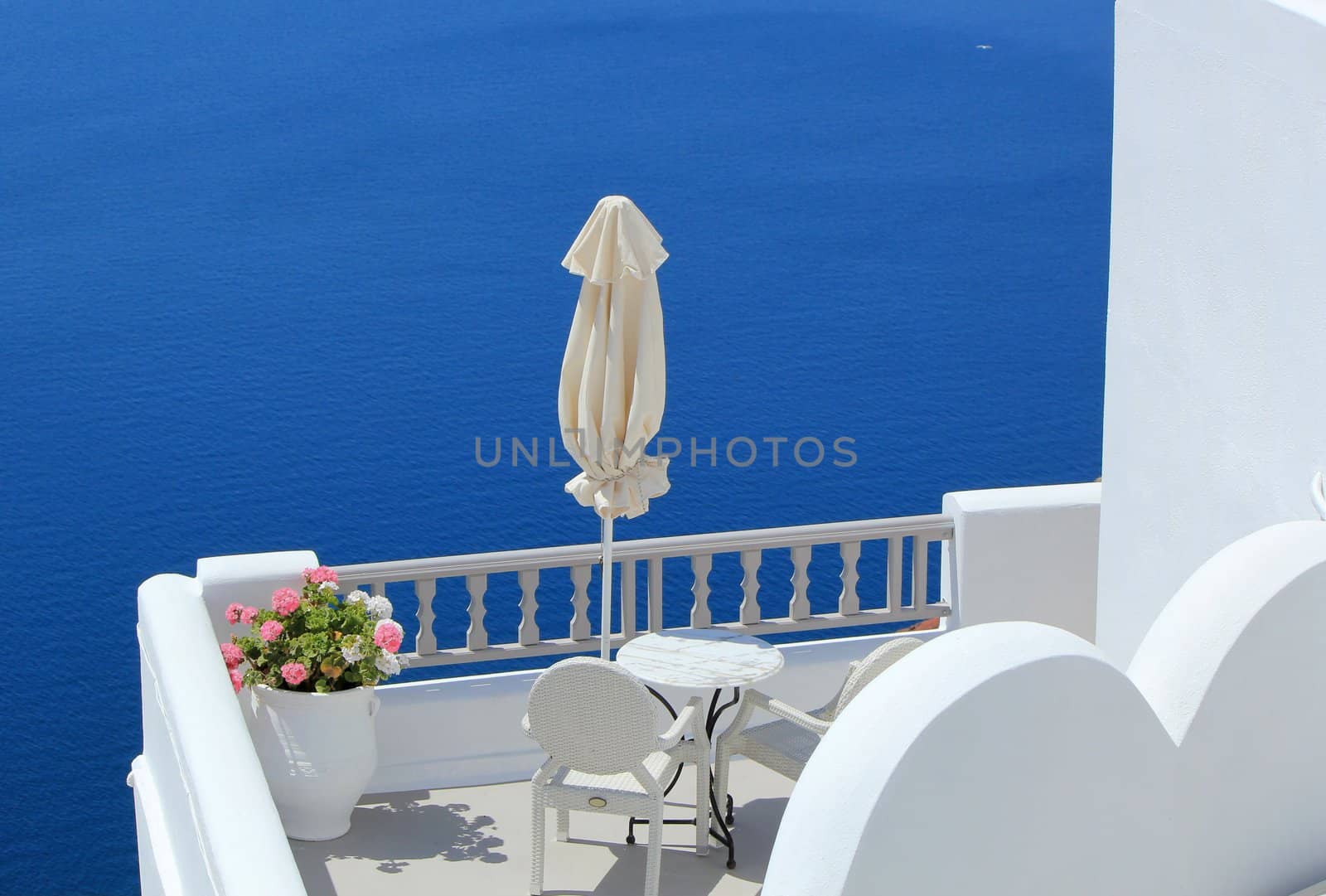 Umbrella, flowers, chairs and table in a white balcony at the sea, Santorini, Greece