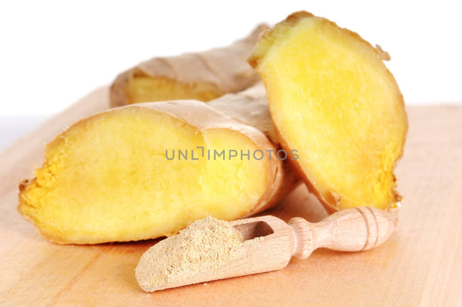 Two cutted ginger roots and small wooden spoon with dry ginger powder. SHallow depth of fields. Focus on dry ginger in the spoon.