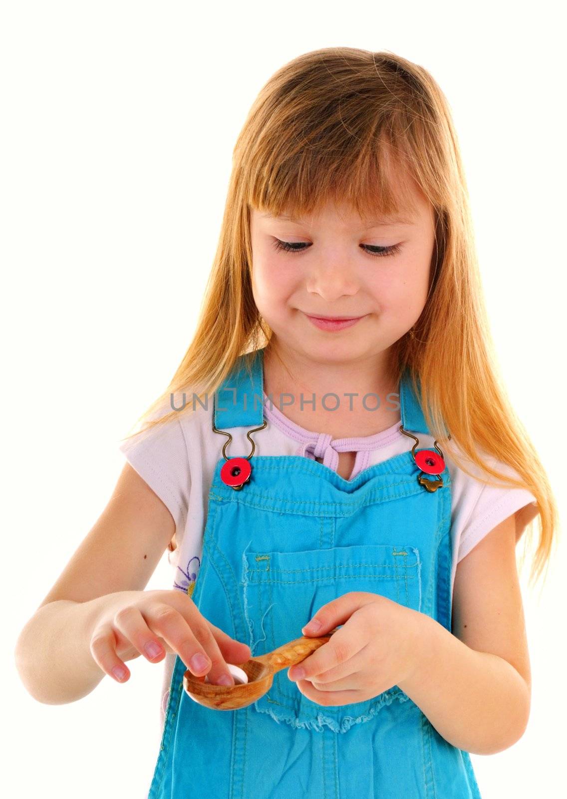 Small beauty girl with one big white tablet in wooden spoon on white background
